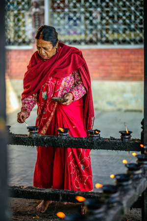 KATHMANDU, NEPAL - OCTOBER 20, 2015 : Elderly woman  lighting candles before prayer in a temple in Kathmanduのeditorial素材