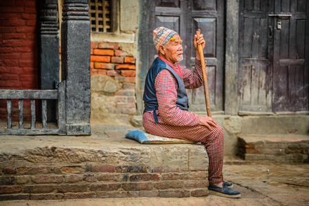 KATHMANDU, NEPAL - OCTOBER 21, 2015 : Elderly beggar with a walking stick sits in the street of Kathmanduのeditorial素材