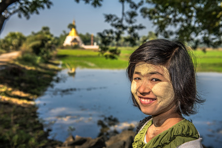 MANDALAY, MYANMAR - JANUARY 20, 2016:  Portrait of a young burmese girl near a buddhist Stupa with thanaka on her face . Thanaka is a yellowish-white cosmetic paste made from ground bark.のeditorial素材