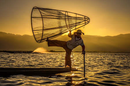 INLE LAKE, MYANMAR - JANUARY 28, 2016 : Burmese fisherman on a traditional bamboo boat catching fish  using a handmade net at sunriseのeditorial素材