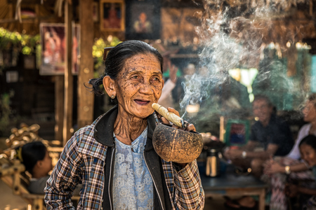 BAGAN, MYANMAR - JANUARY 24, 2016 : Happy and old wrinkled woman smokes  a big cheroot cigar in publicのeditorial素材