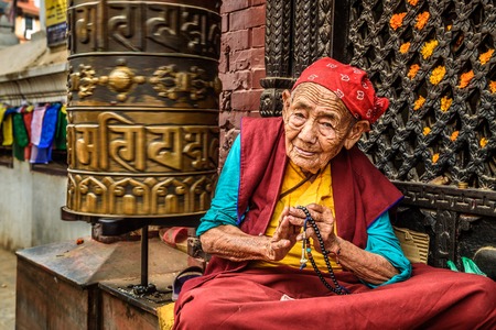 KATHMANDU, NEPAL - OCTOBER 28, 2015 : Very old tibetan buddhist nun sits and begs outside a shrine in Kathmanduのeditorial素材