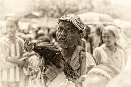 JIMMA, ETHIOPIA - MAY 2, 2015 : Old ethiopian man selling a rooster in a market. Vintage black and white processed.のeditorial素材