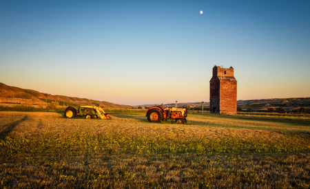 DOROTHY, ALBERTA, CANADA - JULY 6, 2017 : Tractors and abandoned grain elevator in the ghost town of Dorothy in Canada at sunset.のeditorial素材