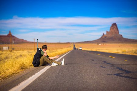 Tired hitch-hiker with suitcase sitting on a roadの写真素材