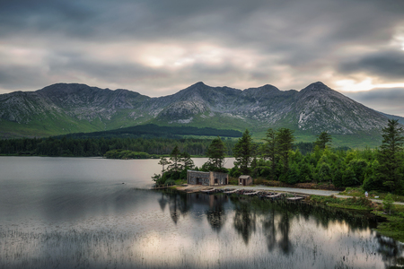 Beautiful lake called Lough Inagh in County Galway, Ireland with a cabin and boats at the lake shore and mountains in the background.の写真素材