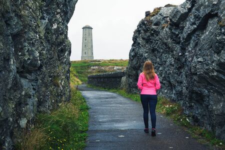 Young woman walking towards Wicklow Head Lighthouse in Irelandの写真素材