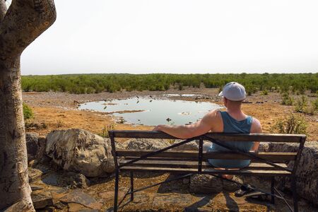 Tourist waits for wildlife at the Moringa waterhole near Halali, Etosha, Namibiaの写真素材