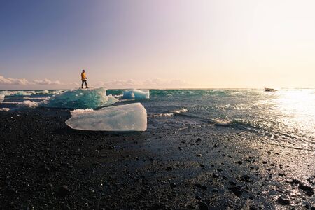 Tourist standing on an iceberg at the Diamond Beach, Iceland