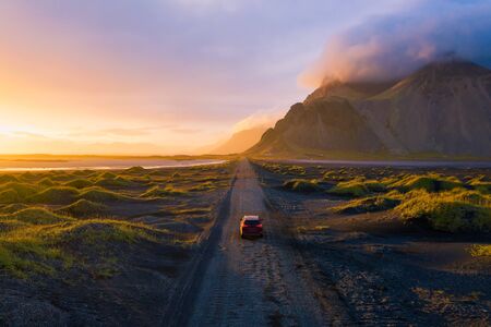 Gravel road at sunset with Vestrahorn mountain and a car driving, Icelandの写真素材
