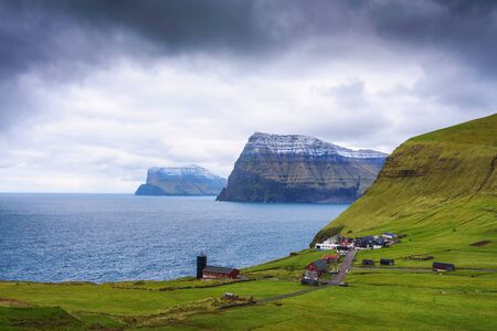 Village of Trollanes located on the island of Kalsoy in Faroe Islands with snow-capped mountains of Kunoy and Bordoy in the backgroundの写真素材