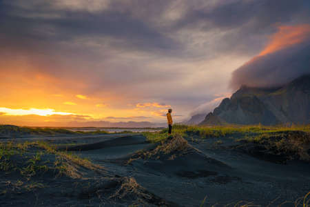 Tourist stands on a sand dune at Vestrahorn mountain in Iceland at sunsetの写真素材