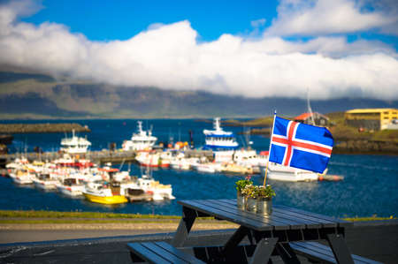 Flag of Iceland placed on a restaurant table with a harbor in the backgroundの写真素材