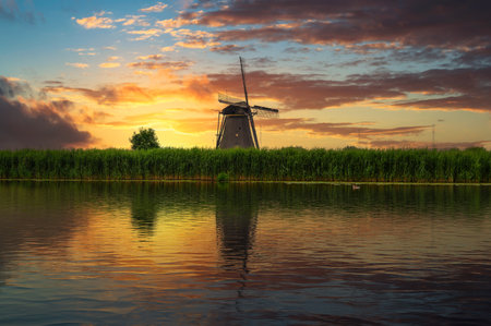 Sunset over an old dutch windmill by a river in Kinderdijk, Netherlandsの写真素材