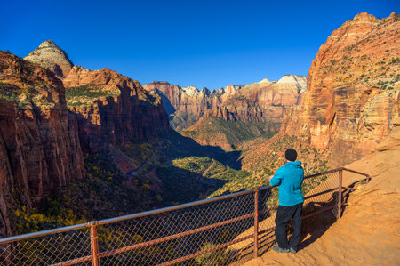A tourist admires the scenic view of Zion Canyon from Canyon Overlook in Zion National Park, Utah, with red cliffs and clear blue skies.の写真素材