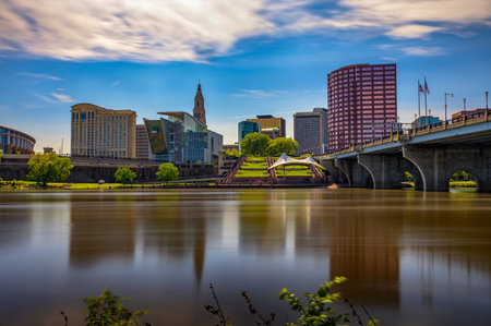 Downtown Hartford, Connecticut, featuring the Founders Bridge across the Connecticut River with a mix of modern and historic buildings, green spaces, and waterfront views. Long exposure.の写真素材