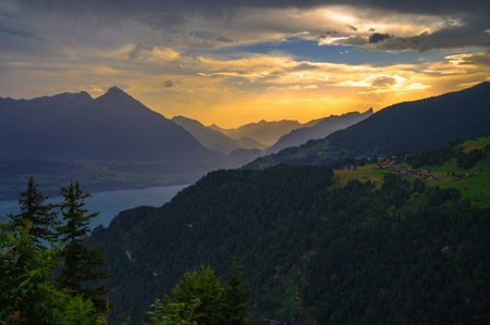 Sunset panorama from Harder Kulm overlooking Thunersee and the surrounding Swiss Alps, with dramatic clouds and lush green valleys in Switzerland.の写真素材
