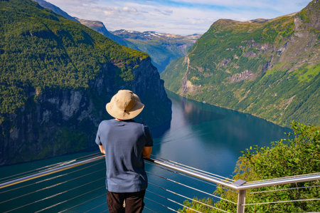 Tourist wearing a sun hat enjoys panoramic view of Geiranger Fjord from a scenic lookout in Norway.の写真素材