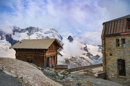 Traditional wooden and stone huts at Gornergrat, Switzerland, with a backdrop of snowy alpine peaks and glaciers.の写真素材