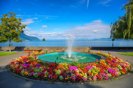 Circular fountain surrounded by vibrant flowers with Lake Geneva and mountains in the background, Villeneuve, Switzerland.の写真素材