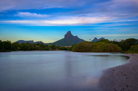 Scenic view of Rempart Mountain from Tamarin Beach, Mauritius, with calm waters in the foreground, lush greenery, and a clear sky at sunset. Long exposure.の写真素材
