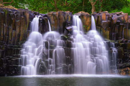 Rochester Falls in Mauritius with water flowing over dramatic basalt rock formations surrounded by lush greenery. Long exposure.の写真素材