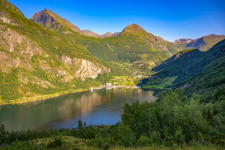 Elevated view of Geiranger village and Geirangerfjord in Norway, surrounded by steep green mountains and calm water.の写真素材