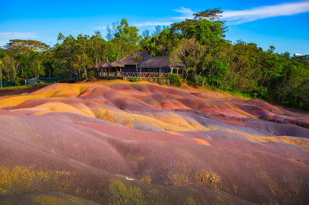 Multicolored sand dunes at Chamarel Seven Colored Earth Geopark with a wooden lodge nestled among trees of a tropical jungle in Mauritius, Africa.の写真素材