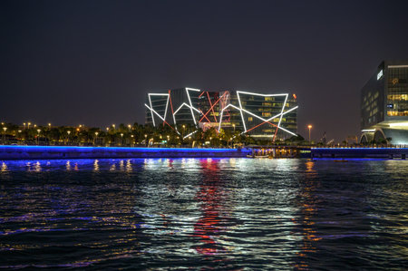Manama, Bahrain - December 27, 2023 : Illuminated Al Baraka Tower and surrounding buildings reflected on Bahrain Bay waters at night in Manama.のeditorial素材