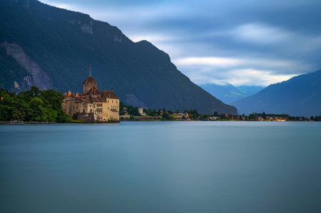 Montreux, Switzerland - July 1, 2024 : Chillon Castle on the edge of Lake Geneva near Montreux, Switzerland, beneath cloudy evening skies and surrounded by Swiss Alps. Long exposure.のeditorial素材