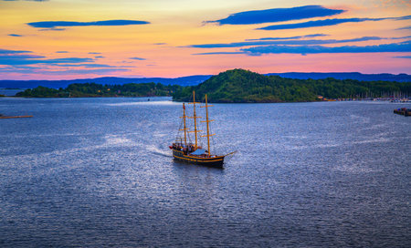 Oslo, Norway - July 30, 2024 : A historic sailing ship cruises Oslo Fjord at sunset, with colorful skies and tree-covered islands in the background.のeditorial素材