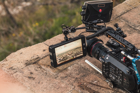 A professional camera is recording the view of a city. The viewfinder is open and showing different video parameters. The camera is placed upon a rock.の写真素材