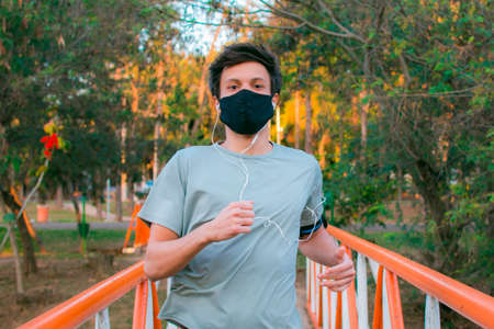 A young man with face mask practicing exercise in the park dressed in sportswear.の写真素材