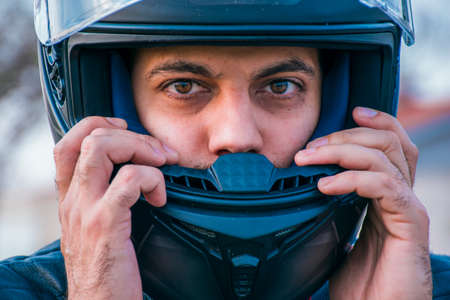 Close-up of the face of a brown-eyed man putting on a motorcycle helmet with his hands.の写真素材