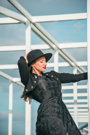 Fashion photography with a young woman with fair skin and blond hair dressed in a long black dress, a black bullfighter and hat.の写真素材