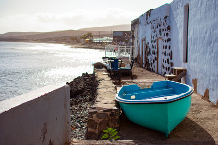 Small green and blue fishing boat, on the ground next to a white house next to the shore of the...