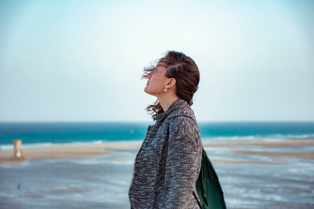 Mature white woman protecting herself from the wind with a linen jacket smiling on Sotavento beach...