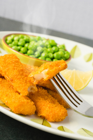 Breaded and Baked Fish Sticks, fingers  on a plate with a bowl of peas and a slice of lemonの写真素材