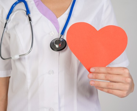 Female doctor with stethoscope holding a red paper heart.の写真素材