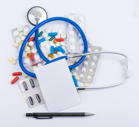 Stethoscope and a blank sheet of paper mixed in a pile of pillsの写真素材