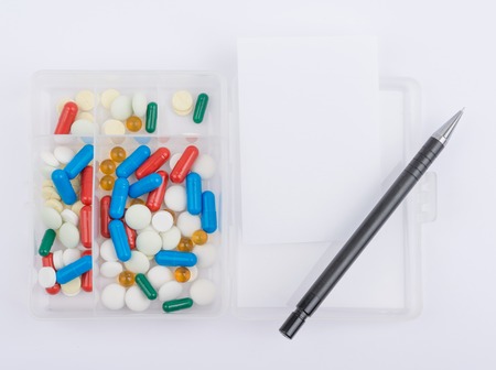 Pills in capsules in glass box with white paper sheet and ballpoint pen.の写真素材