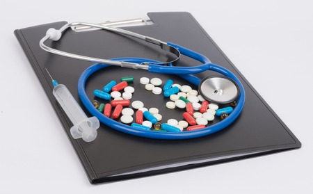 Medical stethoscope and pills lie on clipboard.の写真素材