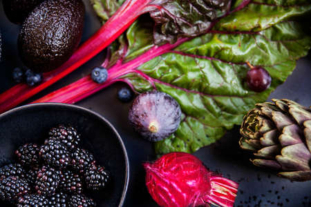 Mix of purple raw vegetables and fruits on black background and blackberries on a bowl. Figs,...