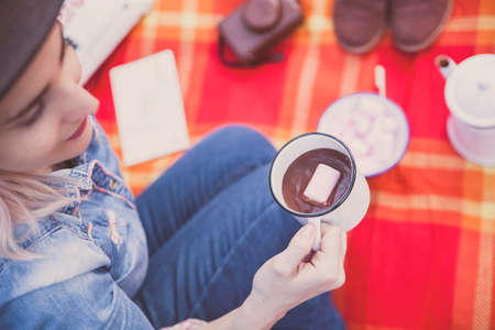 Top view of a girl enjoying a cup of hot cocoa and a marshmallow outdoors, on a picnic blanket