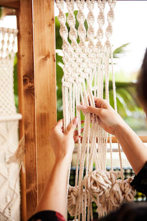 Detail of a macrame pattern and the hands of a girl making knots with the ropes. She has a manicure...