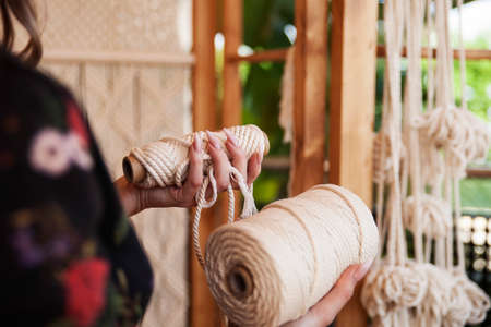 Girl with long nails holds two rolls of macrame rope. Close-up of hands.の写真素材