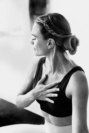 A woman with braids in her hair is meditating in a yoga studio with her hand over her heart. She wears sportswear and braids.の写真素材