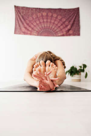 She is bent on the floor holding her feet with her hands in gyan mudra