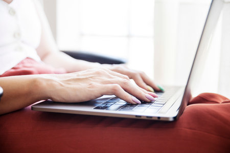 Close up shot of a young woman`s hands typing on her laptop. She has long nails and a manicure doneの写真素材