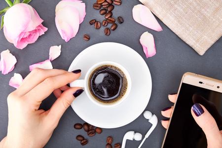 Womans hand holding cup of coffee and smartphone.の写真素材